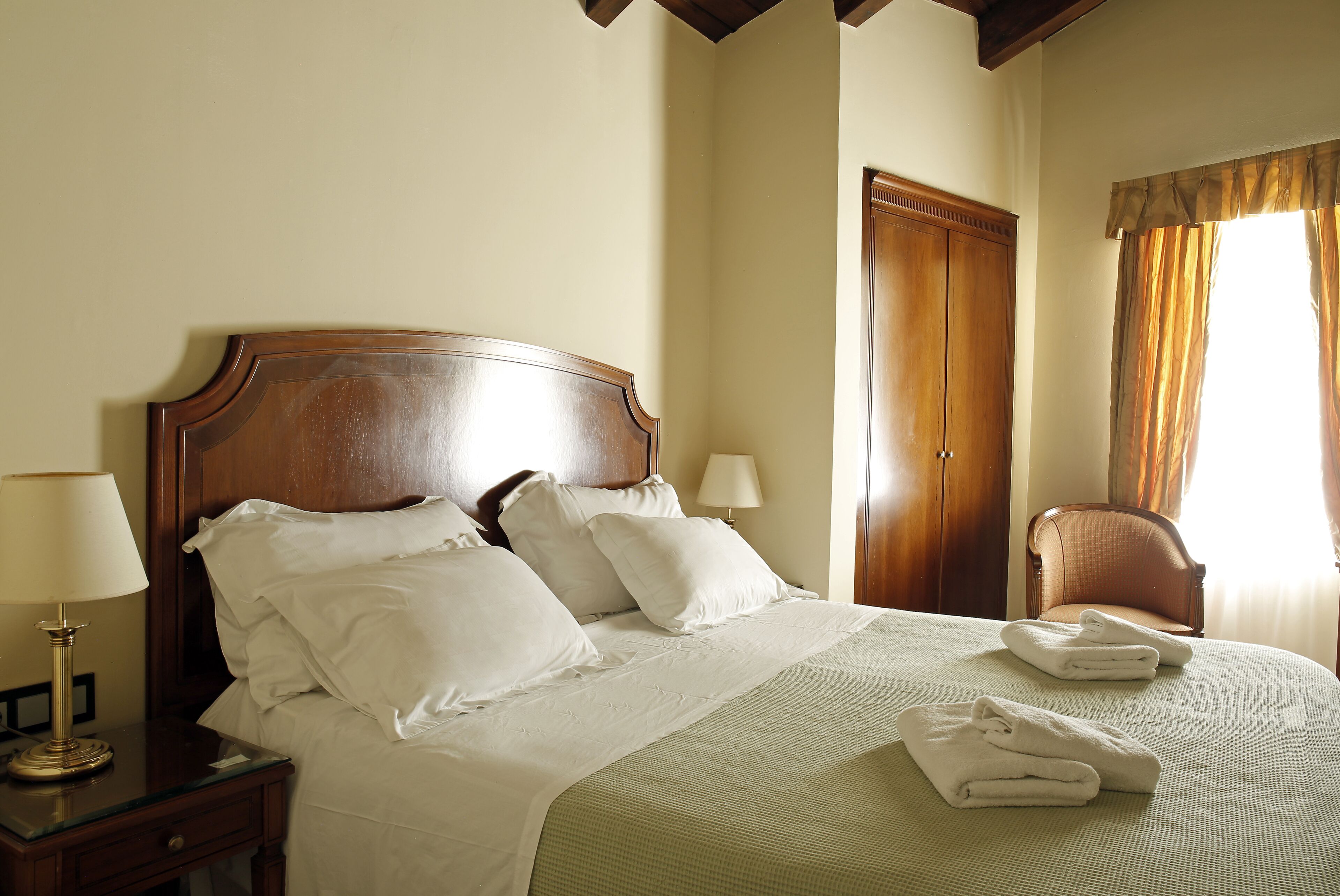 A neatly made bed with white linens and pillows, a wooden headboard, and a bedside table with a lamp.
