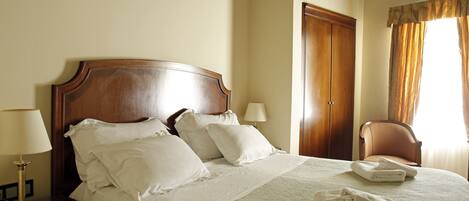 A neatly made bed with white linens and pillows, a wooden headboard, and a bedside table with a lamp.