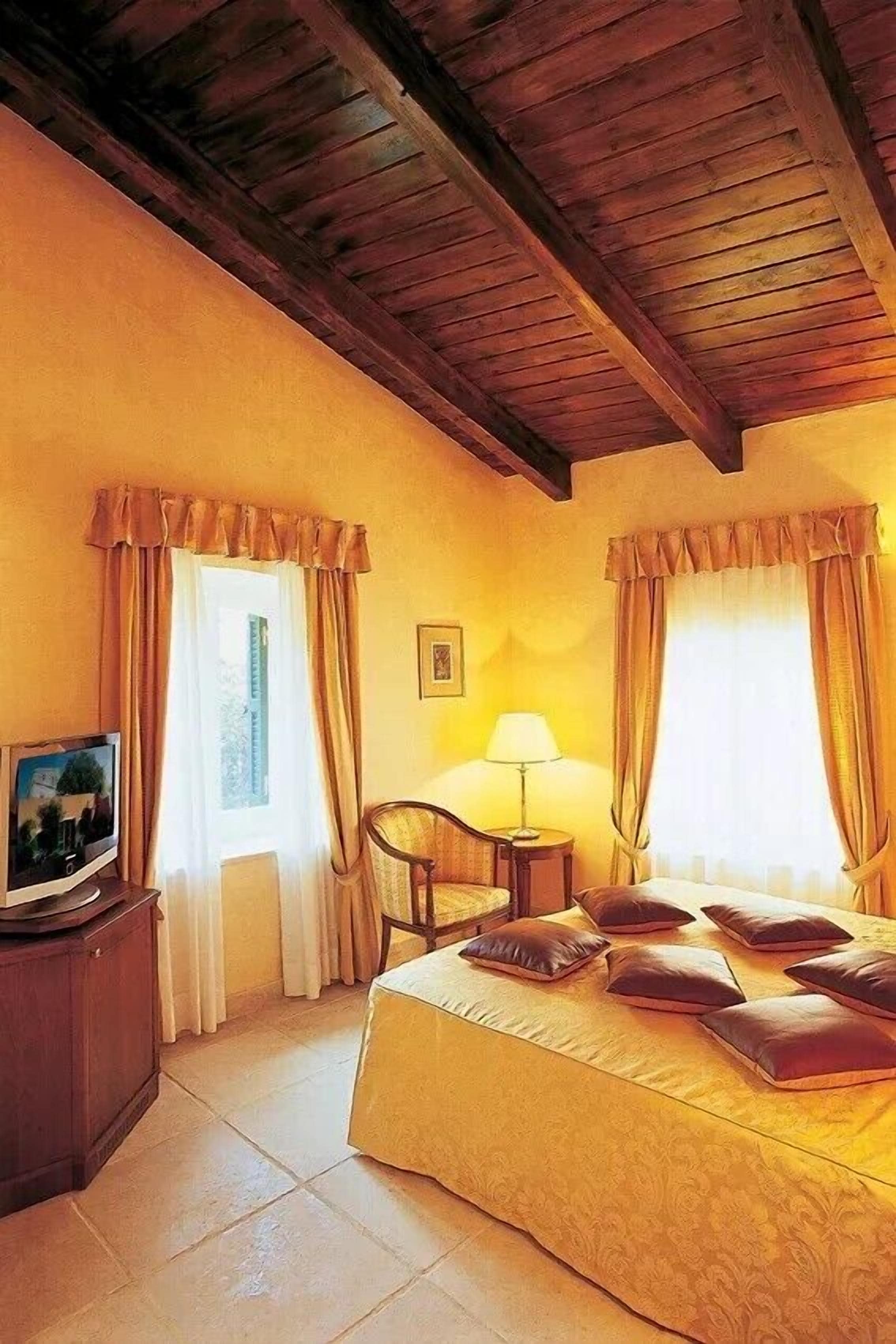 A hotel room with a bed, a television, a chair, a lamp, and curtains.