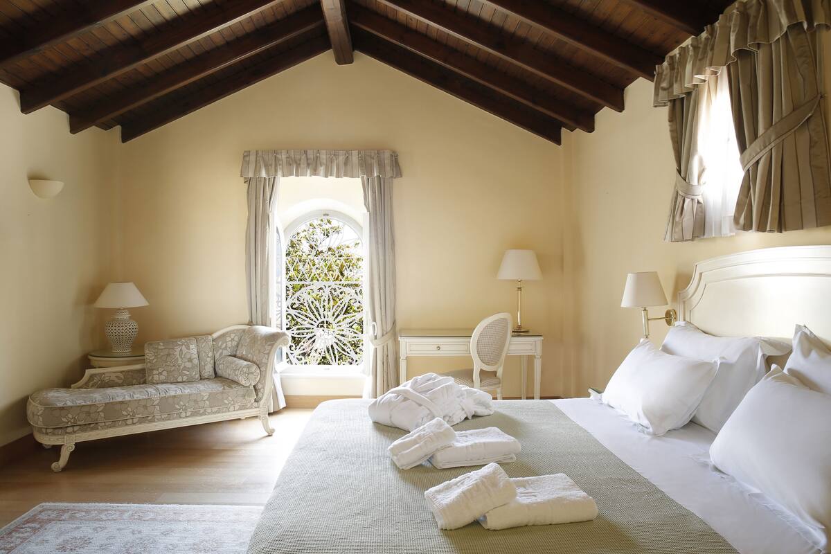 Una camera da letto con un letto, due comodini con lampade, un divano e una finestra con tende.