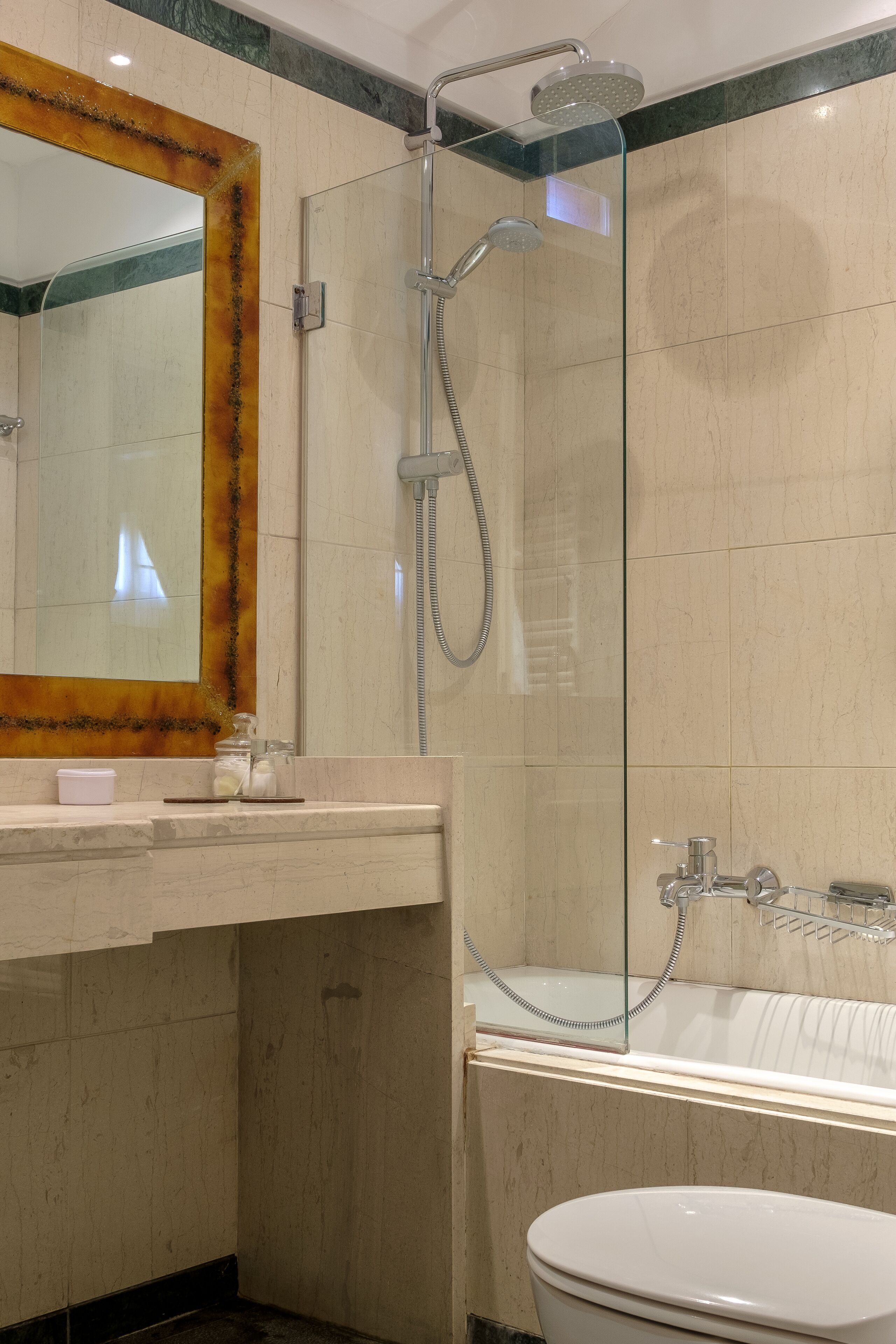 Un baño con ducha envuelta en cristal, inodoro blanco y pared con azulejos de mármol.