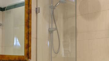 Un baño con ducha envuelta en cristal, inodoro blanco y pared con azulejos de mármol.