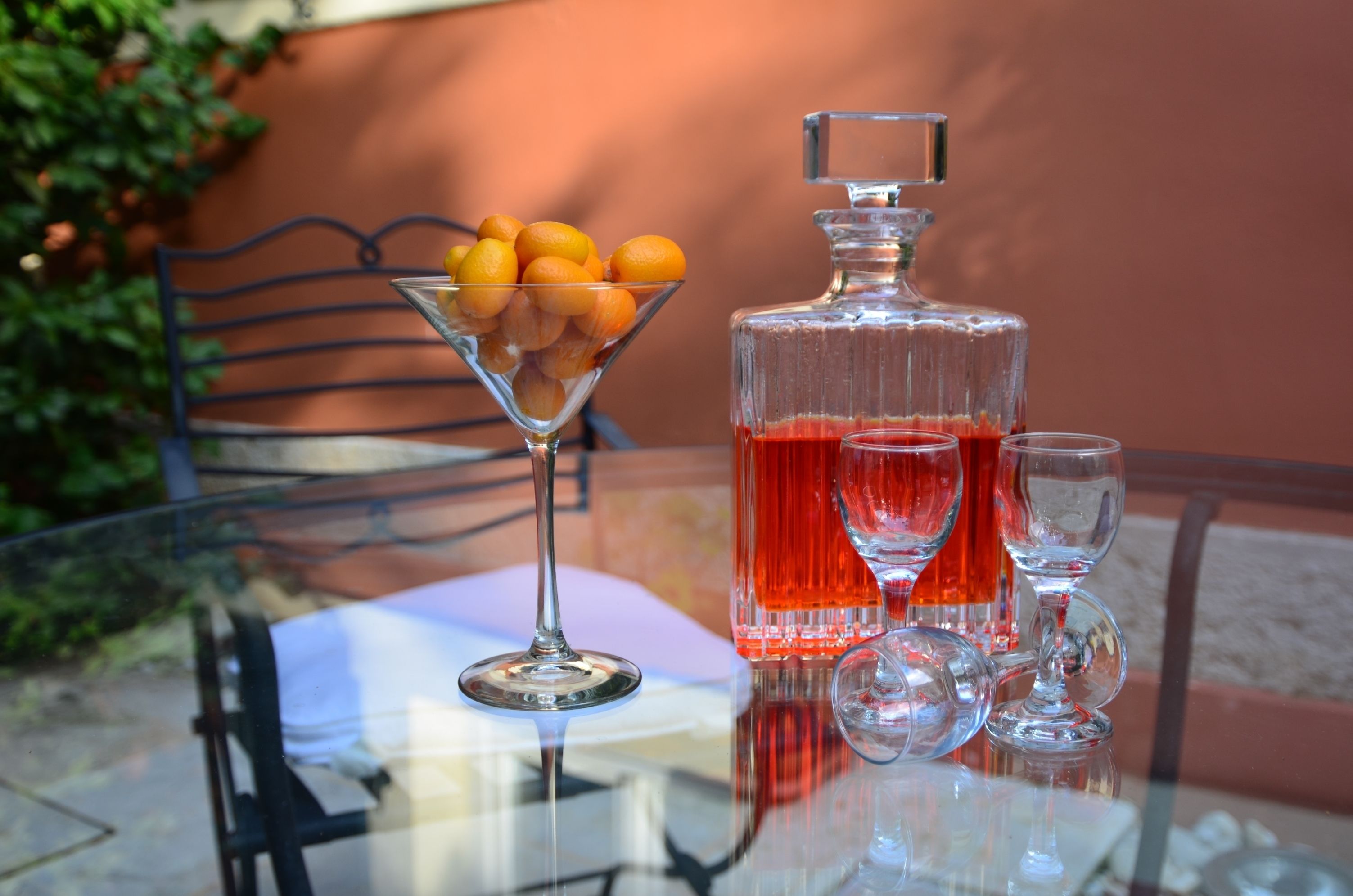 Een glazen tafel met een martini-glas, een decanter en twee wijnglazen gevuld met rode vloeistof.