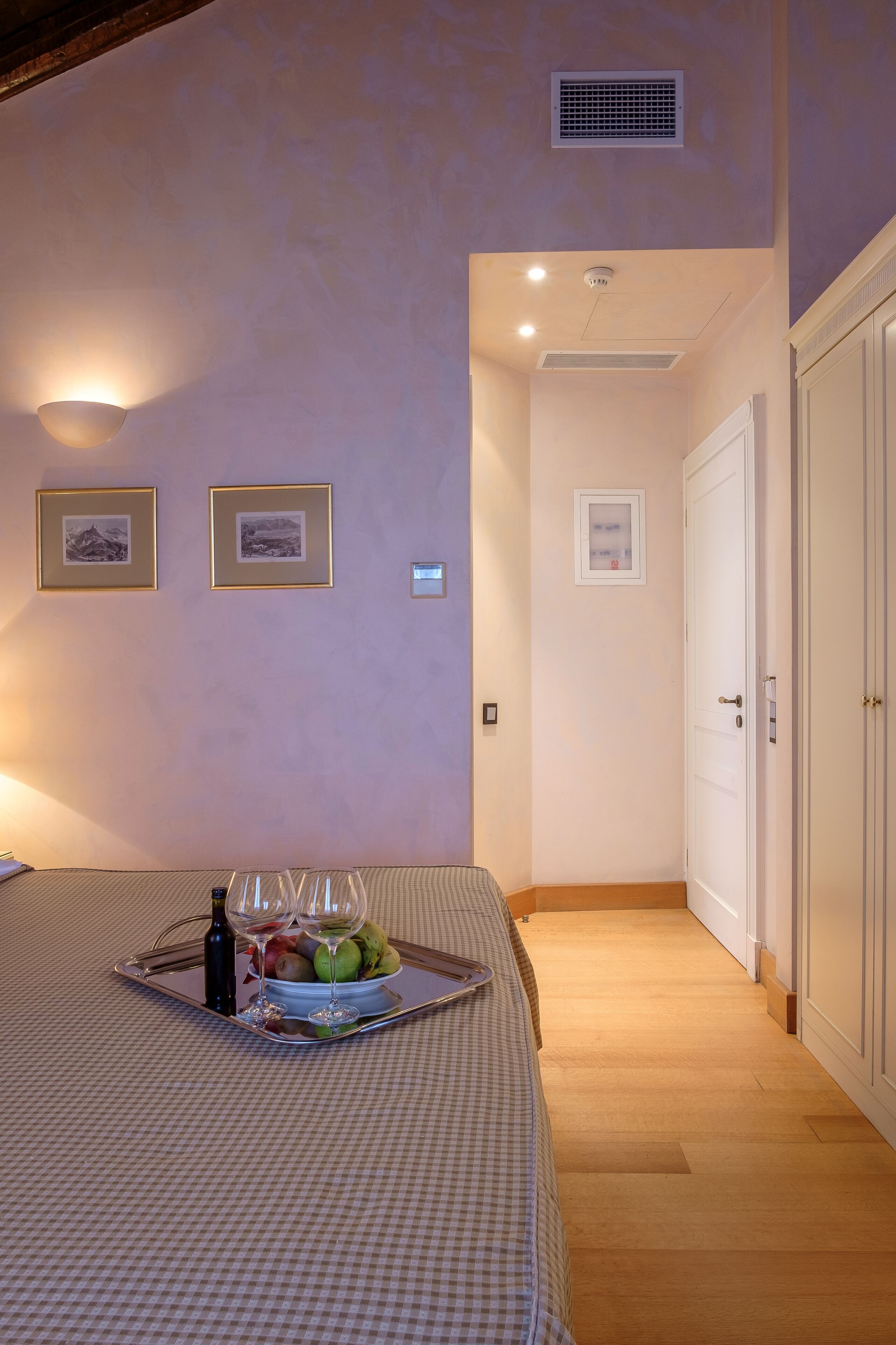Un dormitorio con una cama, una bandeja con frutas y copas de vino, y cuadros en la pared.