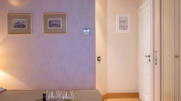 Un dormitorio con una cama, una bandeja con frutas y copas de vino, y cuadros en la pared.