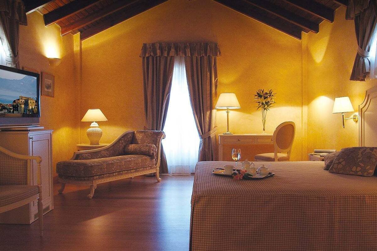 Una camera d'albergo accogliente con un letto grande, un divano, due lampade, un tavolino e una televisione su un mobile.