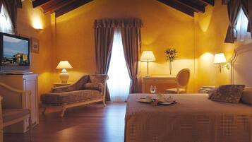 Una habitación de hotel acogedora con una cama grande, un sofá, dos lámparas, una mesita y un televisor sobre un mueble.
