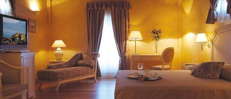 A cozy hotel room with a large bed, a sofa, two lamps, a small table, and a television on a cabinet.