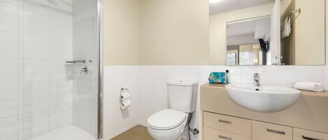 Un baño moderno con cabina de ducha de vidrio, inodoro blanco y tocador color beige con lavamanos y espejo.