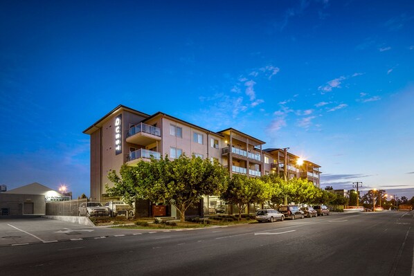 A multi-story hotel with balconies, a parking lot, and trees in front.