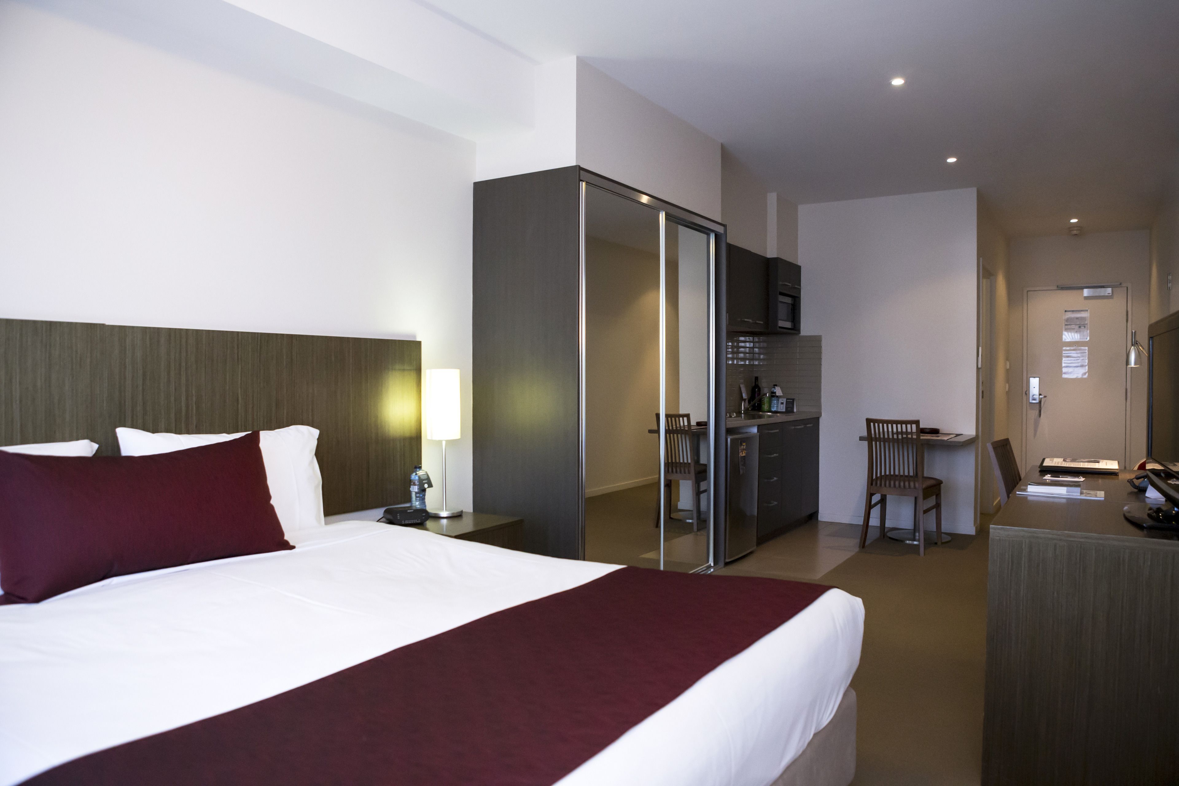 A hotel room with a large bed, a desk, a chair, a minibar, and a separate bathroom area.