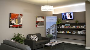 Una moderna zona de recepción con un sofá, una mesa de centro, un televisor y una estantería con folletos.