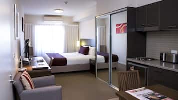 Habitación de hotel con cama, escritorio, silla, pequeña kitchenette y puerta corredera que da al baño.