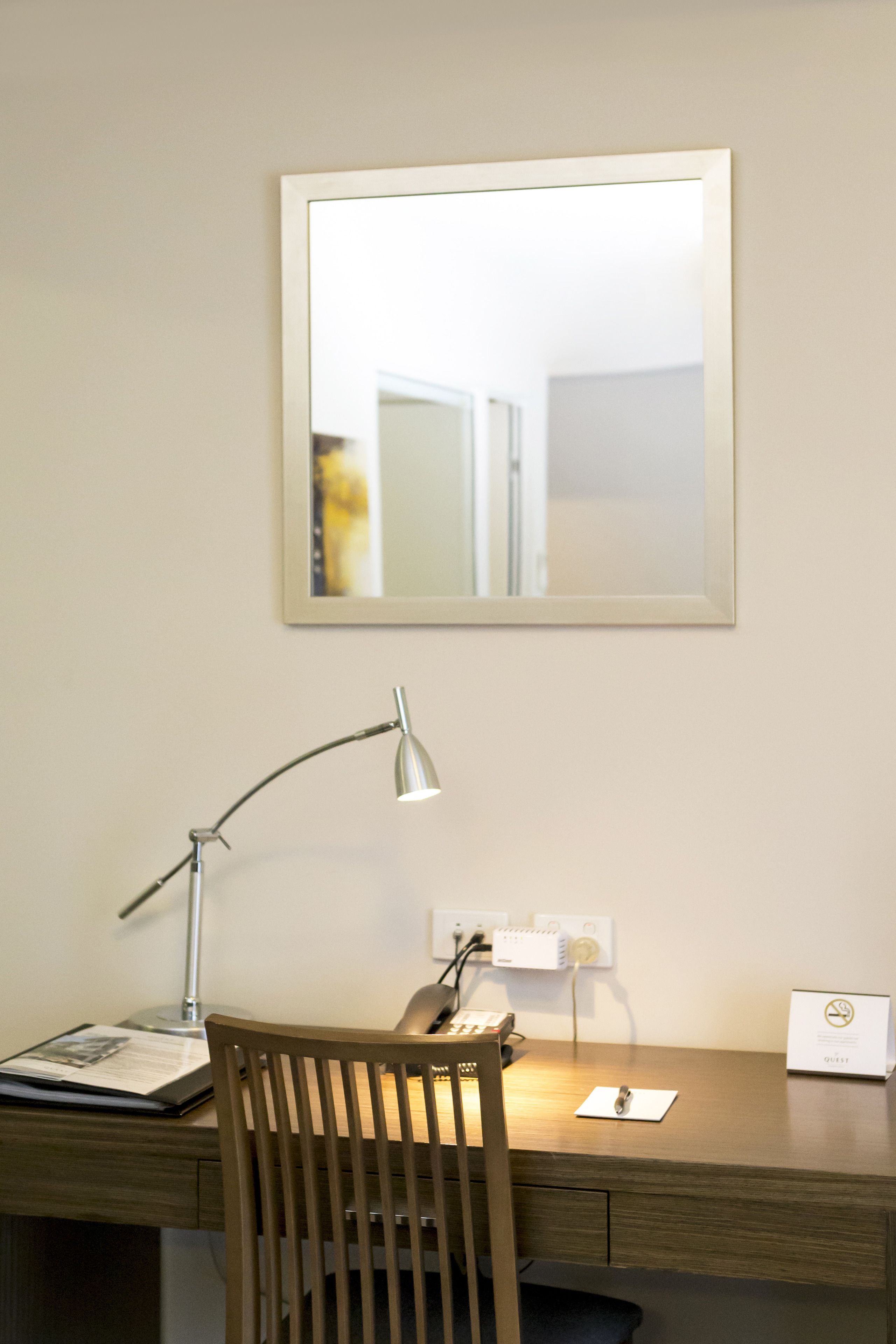 A wooden desk with a lamp, a chair, a mirror, and a sign on the wall.
