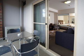 A hotel room with a glass door leading to a balcony, a bed, a sofa, a table, and chairs.