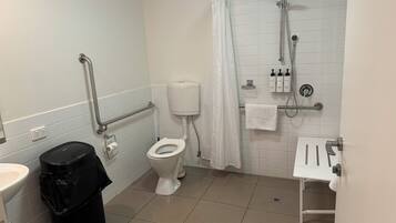 Ein Badezimmer mit Toilette, Dusche und Waschbecken. Ein Mülleimer und ein Handtuchhalter sind ebenfalls vorhanden.