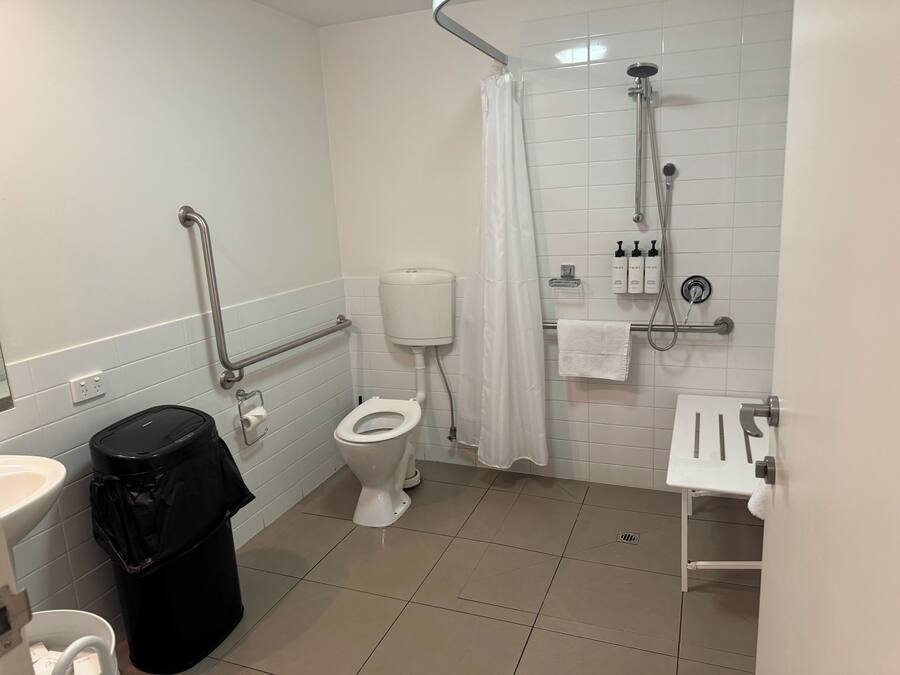 Ein Badezimmer mit Toilette, Dusche und Waschbecken. Ein Mülleimer und ein Handtuchhalter sind ebenfalls vorhanden.