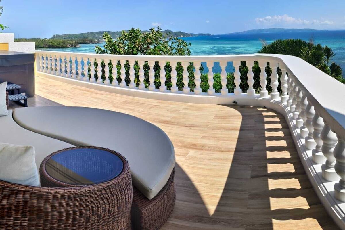 Un espacio de descanso al aire libre con sillón de mimbre y cojines, jacuzzi y vistas al océano.