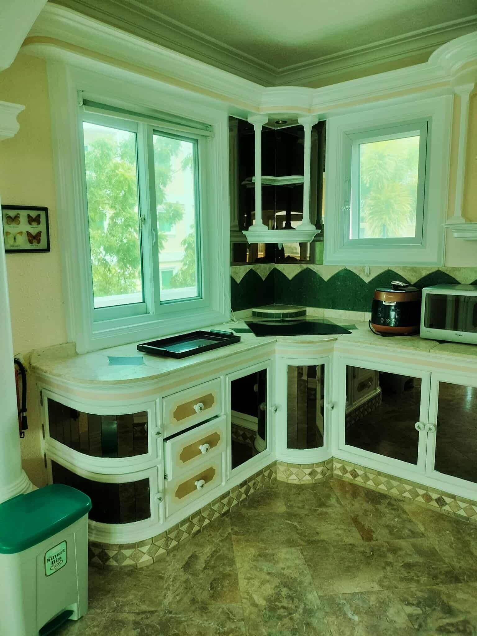A kitchen with a curved countertop, a microwave, and a sink. There are two windows providing natural light.
