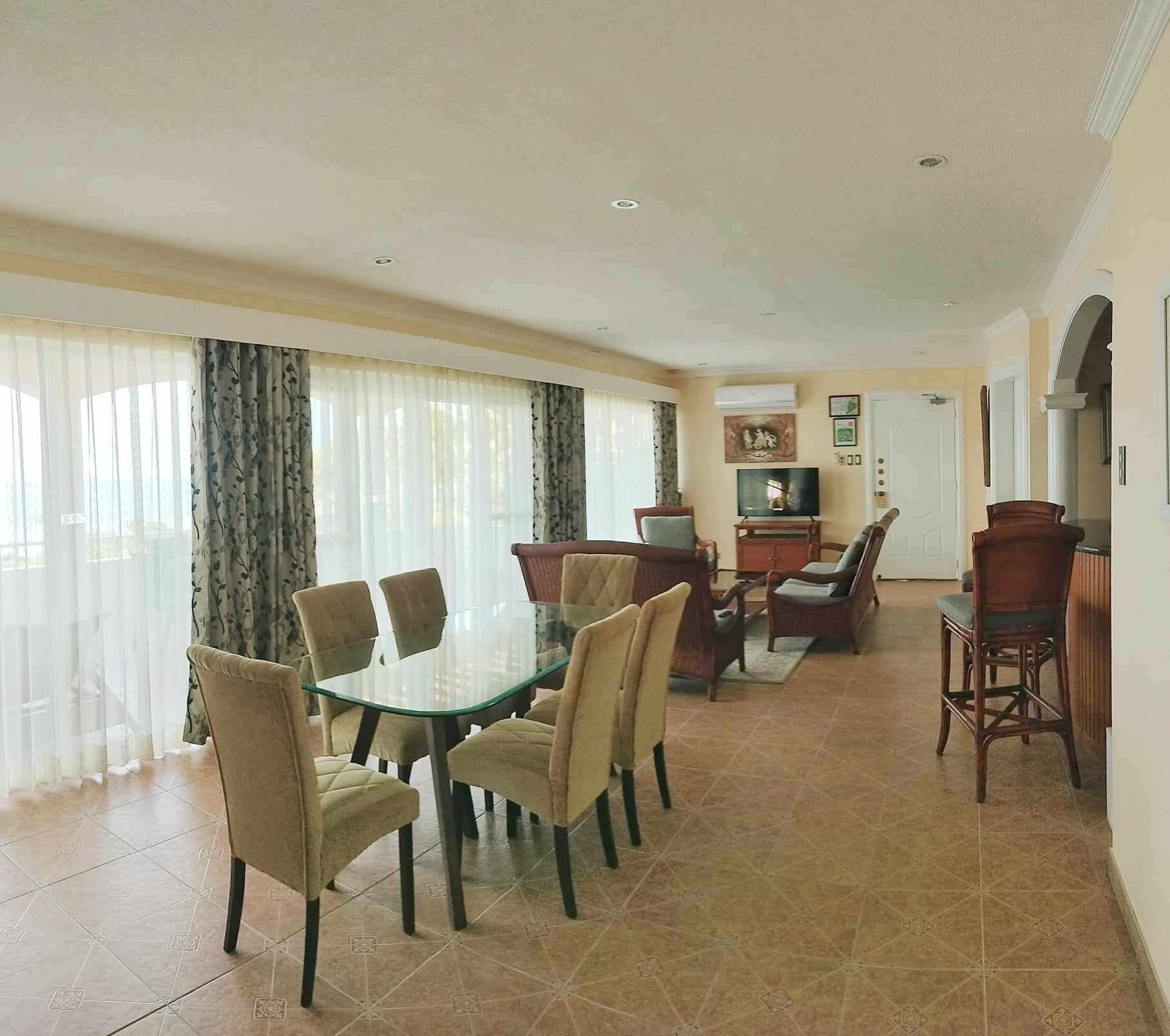 Un coin repas avec une table en verre entourée de chaises, un téléviseur et une porte au fond.