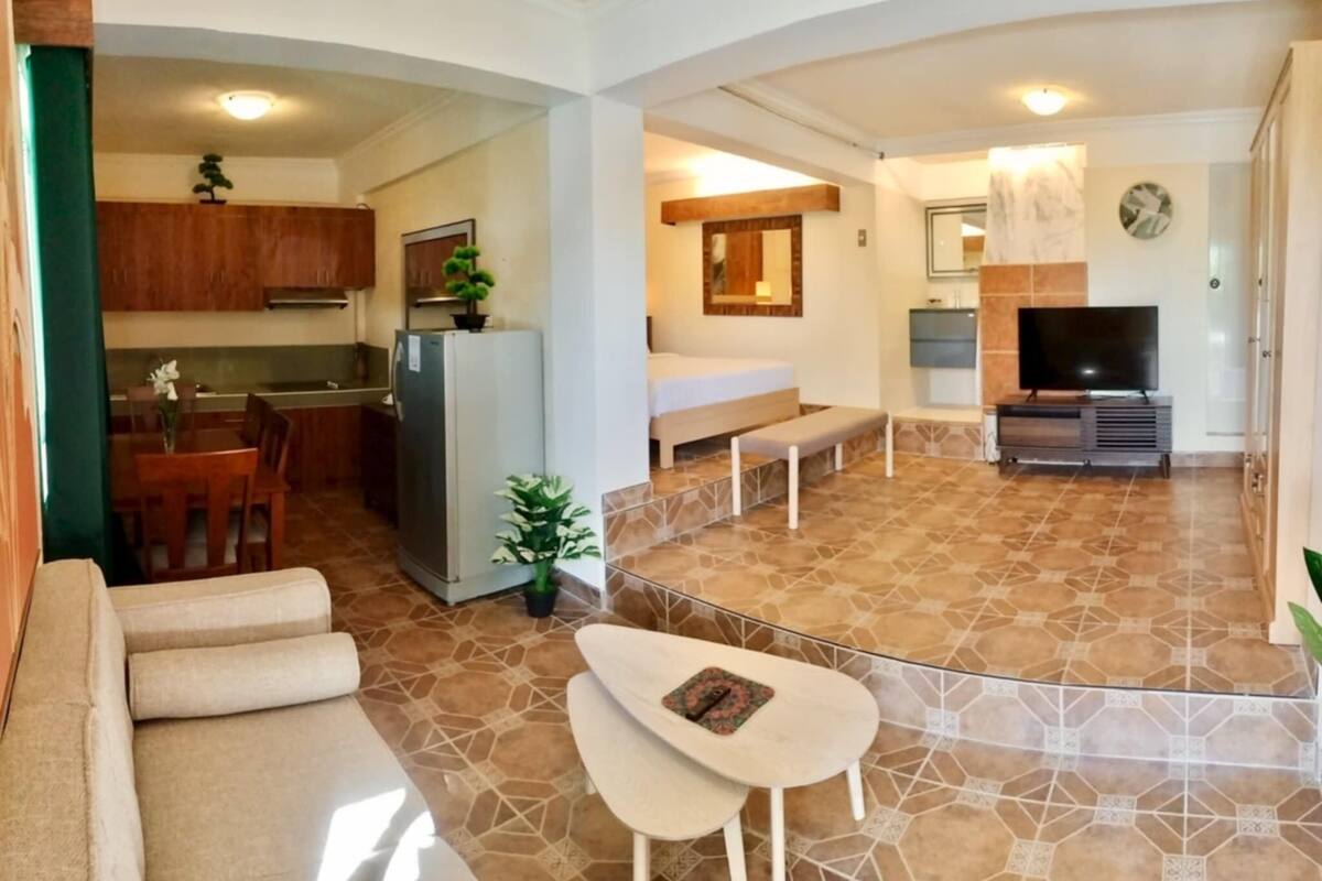 Una sala de estar moderna con un sofá, una mesita, un televisor y una cocina con armarios y un refrigerador.