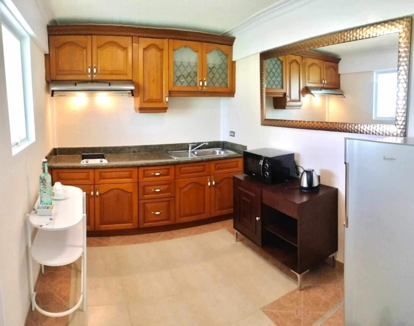 Una cocina con armarios de madera, microondas integrado, fregadero y refrigerador.