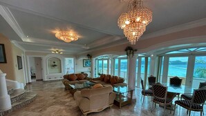 Een ruime woonkamer met een grote zithoek, een glazen tafel en uitzicht op de oceaan.