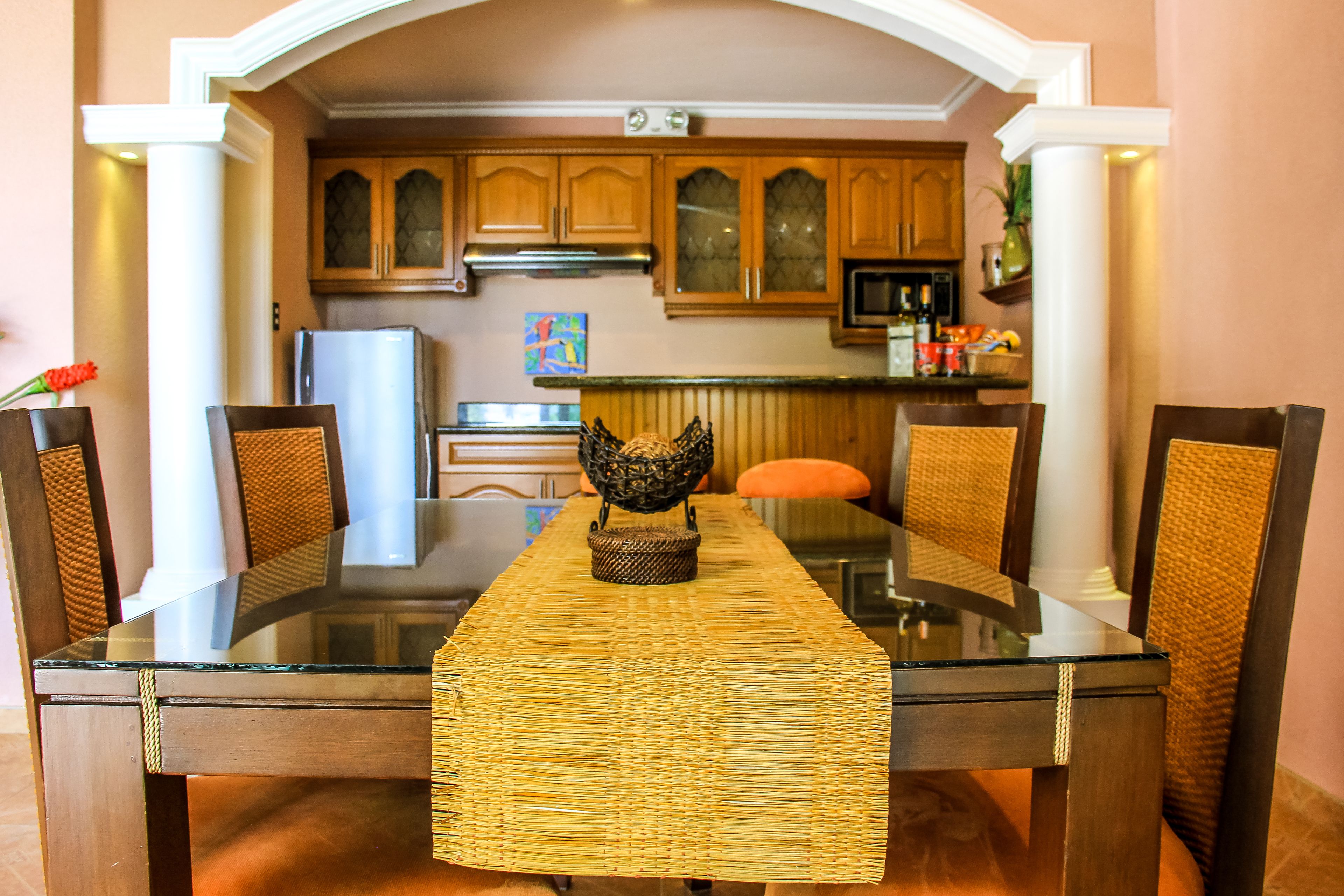 A dining table with a woven table runner, surrounded by chairs with woven backs.