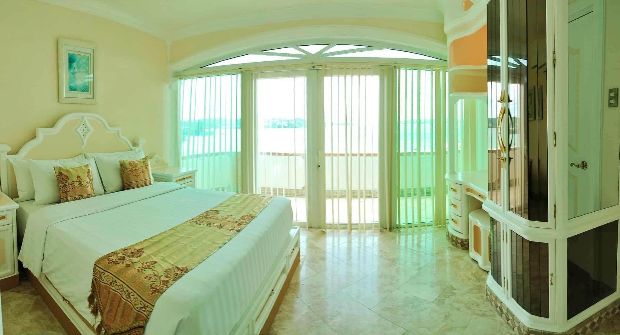A bedroom with a large bed, a nightstand, a wardrobe, and a balcony with glass doors.