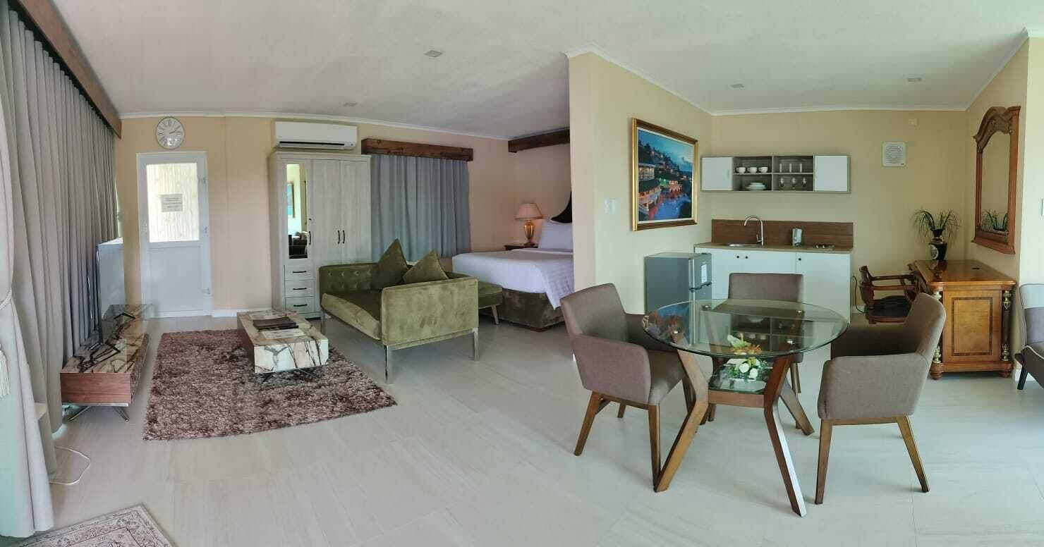 Een moderne woonkamer met een glazen eettafel, een bank, een bed en een keukenhoek.