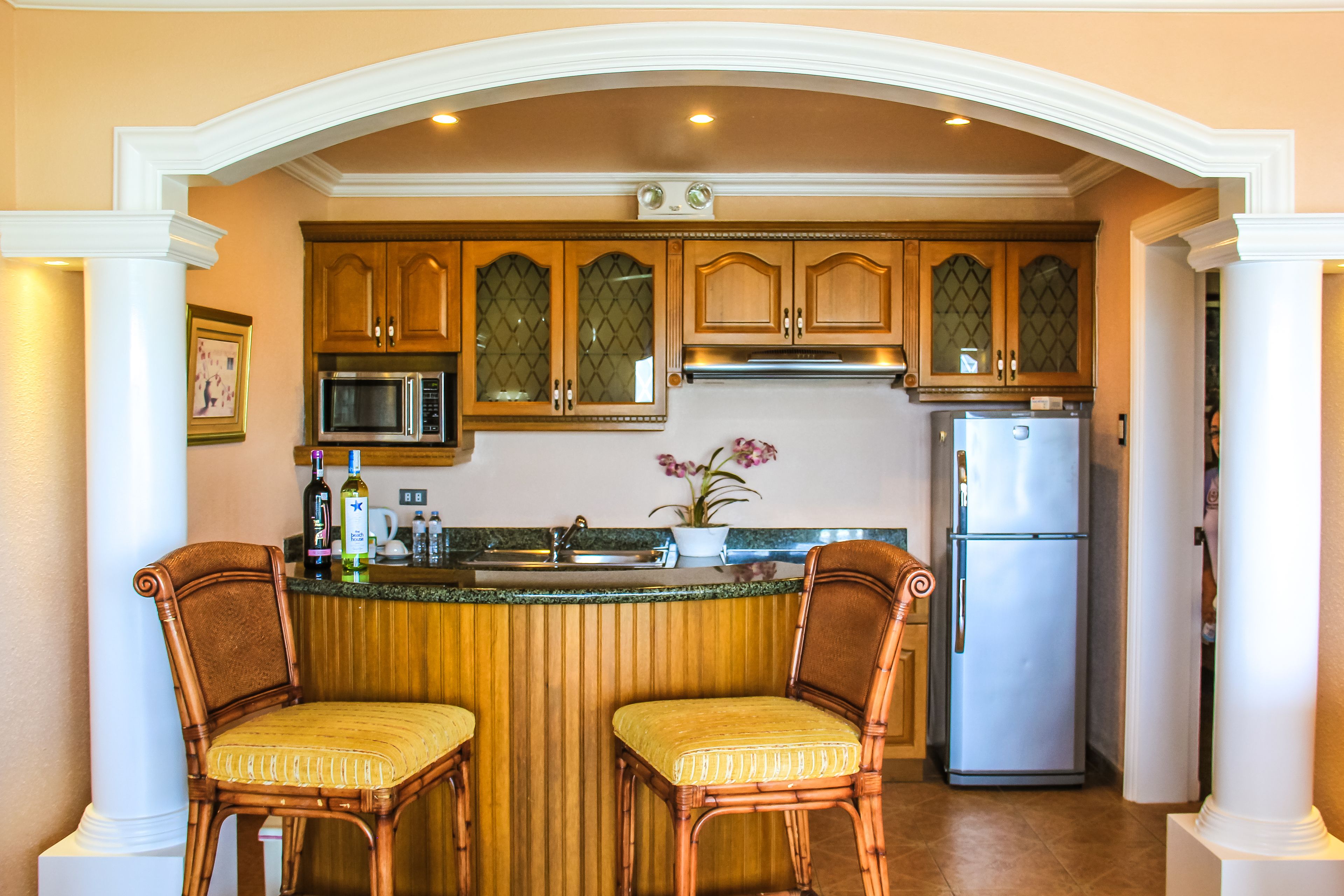 Una cocina con armarios de madera, un refrigerador de acero inoxidable y dos sillas de mimbre.