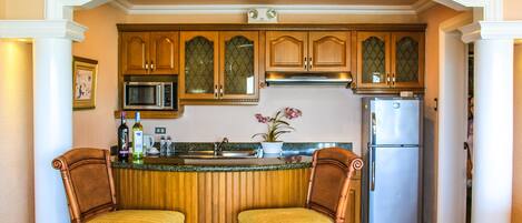 Una cocina con armarios de madera, un refrigerador de acero inoxidable y dos sillas de mimbre.