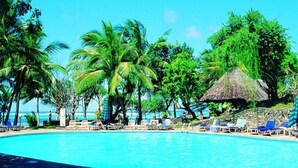 A pool area with lounge chairs and umbrellas, surrounded by palm trees and a thatched structure. - Kaskazi Beach Hotel (Diani Beach)