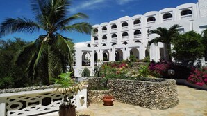A white building with multiple arches and a stone wall. - Kaskazi Beach Hotel (Diani Beach)