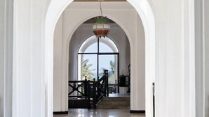 A spacious hallway with white walls and tiled floors, leading to a balcony with a view of palm trees. - Kaskazi Beach Hotel (Diani Beach)