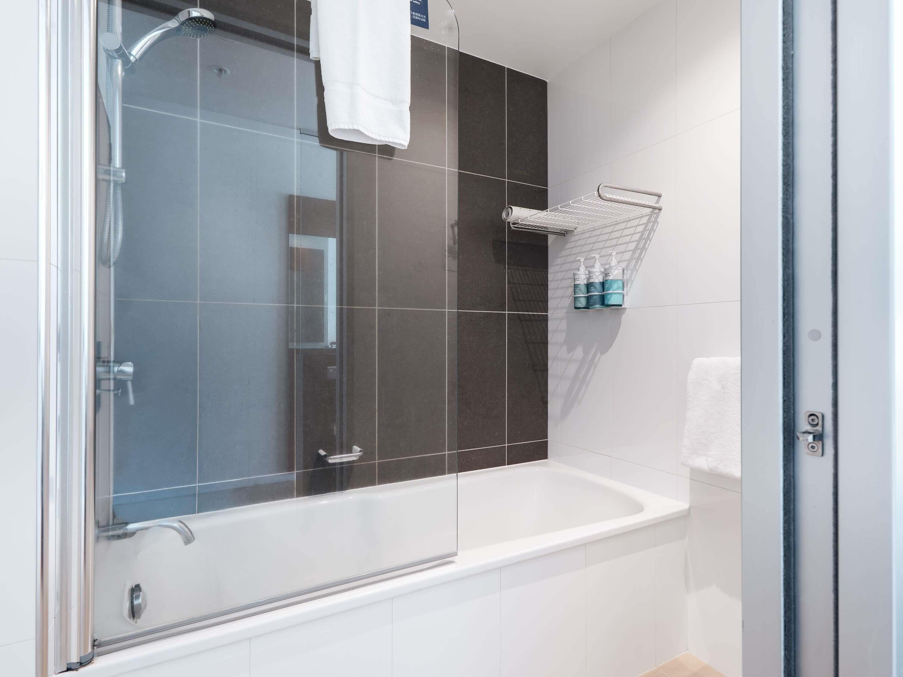 A modern bathroom with a glass-enclosed shower, a white bathtub, and a towel rack with toiletries.