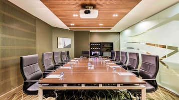 A conference room with a long table, black leather chairs, a projector, and a television.