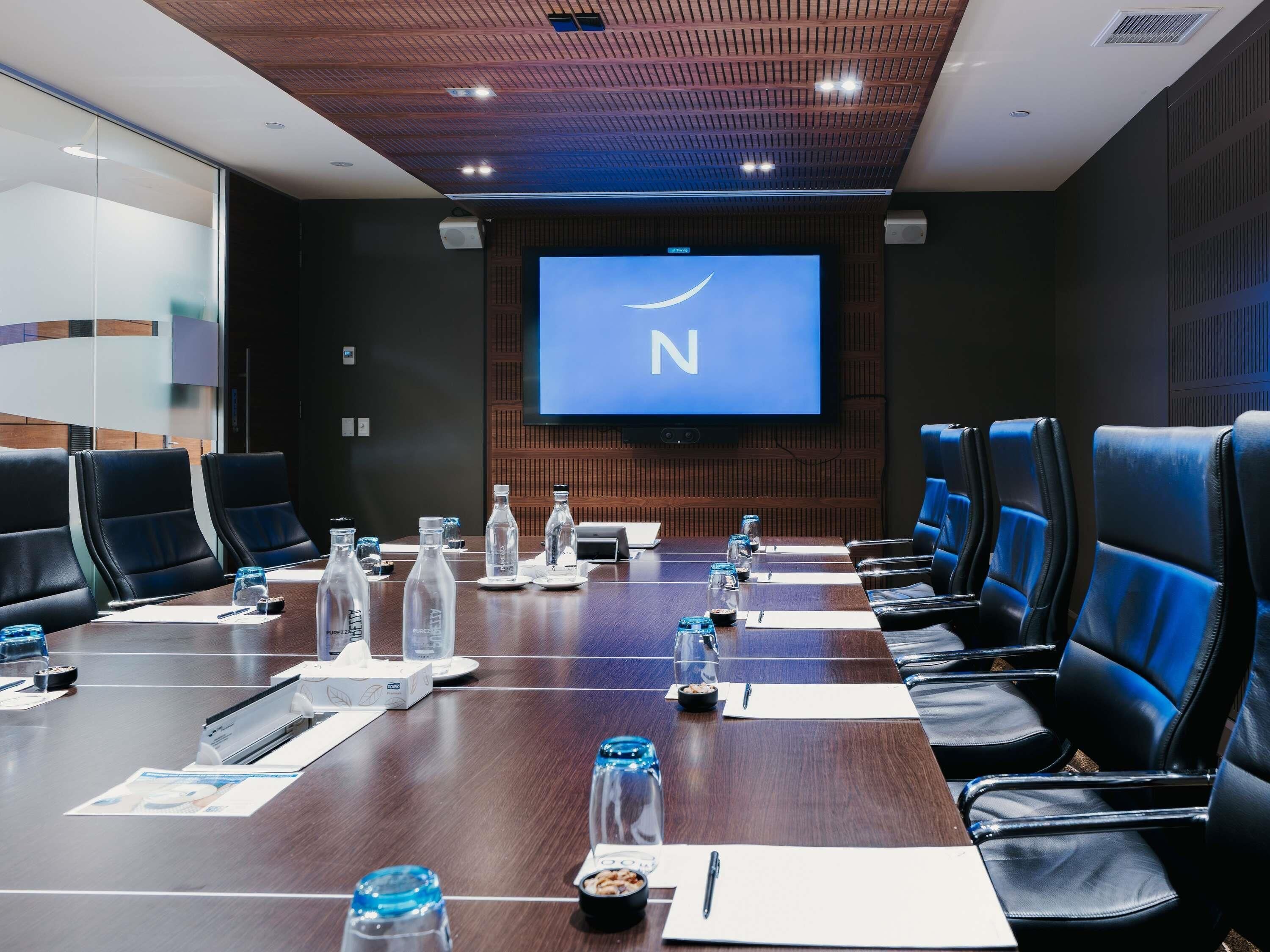 Une salle de conférence équipée d’une longue table, de chaises, d’un écran de projection et d’un téléviseur.