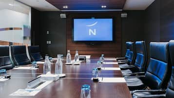 A conference room with a long table, chairs, a projector screen, and a television.