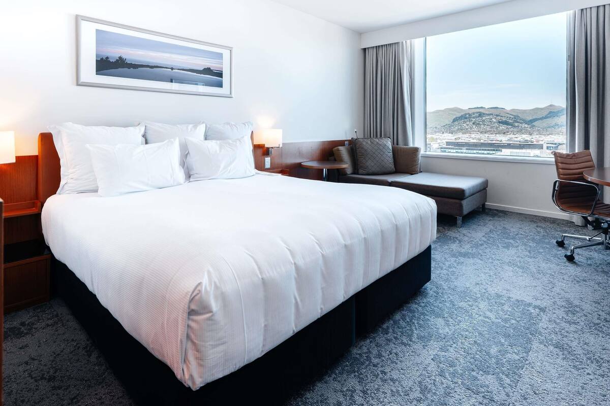 Ein Hotelzimmer mit einem großen Bett, einer Sitzecke, einem Schreibtisch und Blick auf die Stadt.