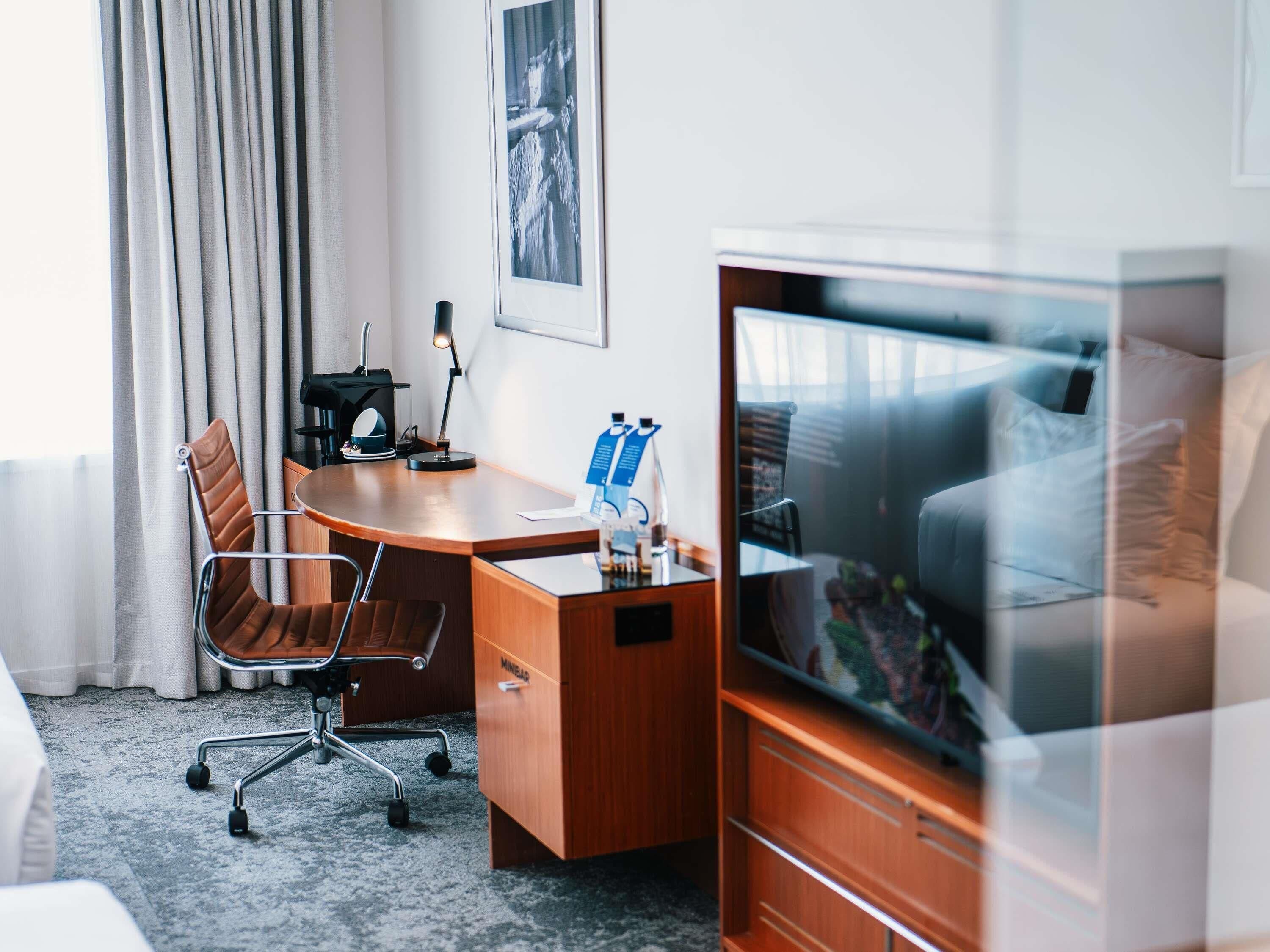 Une chambre d’hôtel avec un bureau en bois, une chaise, un lit, une télévision et un tableau encadré au mur.