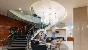 A modern hotel lobby with a staircase, seating area, and a chandelier. - Novotel Christchurch Cathedral Square (Christchurch)