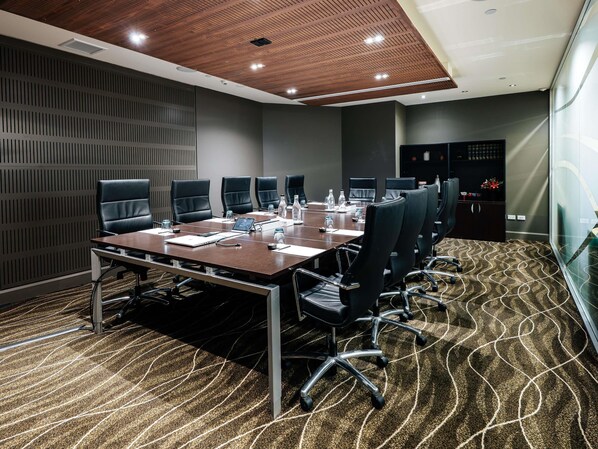 A conference room with a long table, black chairs, a wooden ceiling, and a patterned carpet.