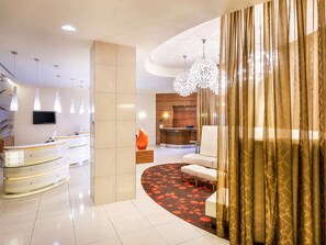 Eine moderne Hotelhalle mit Empfangstresen, Sitzgelegenheiten und einem großen Kronleuchter.