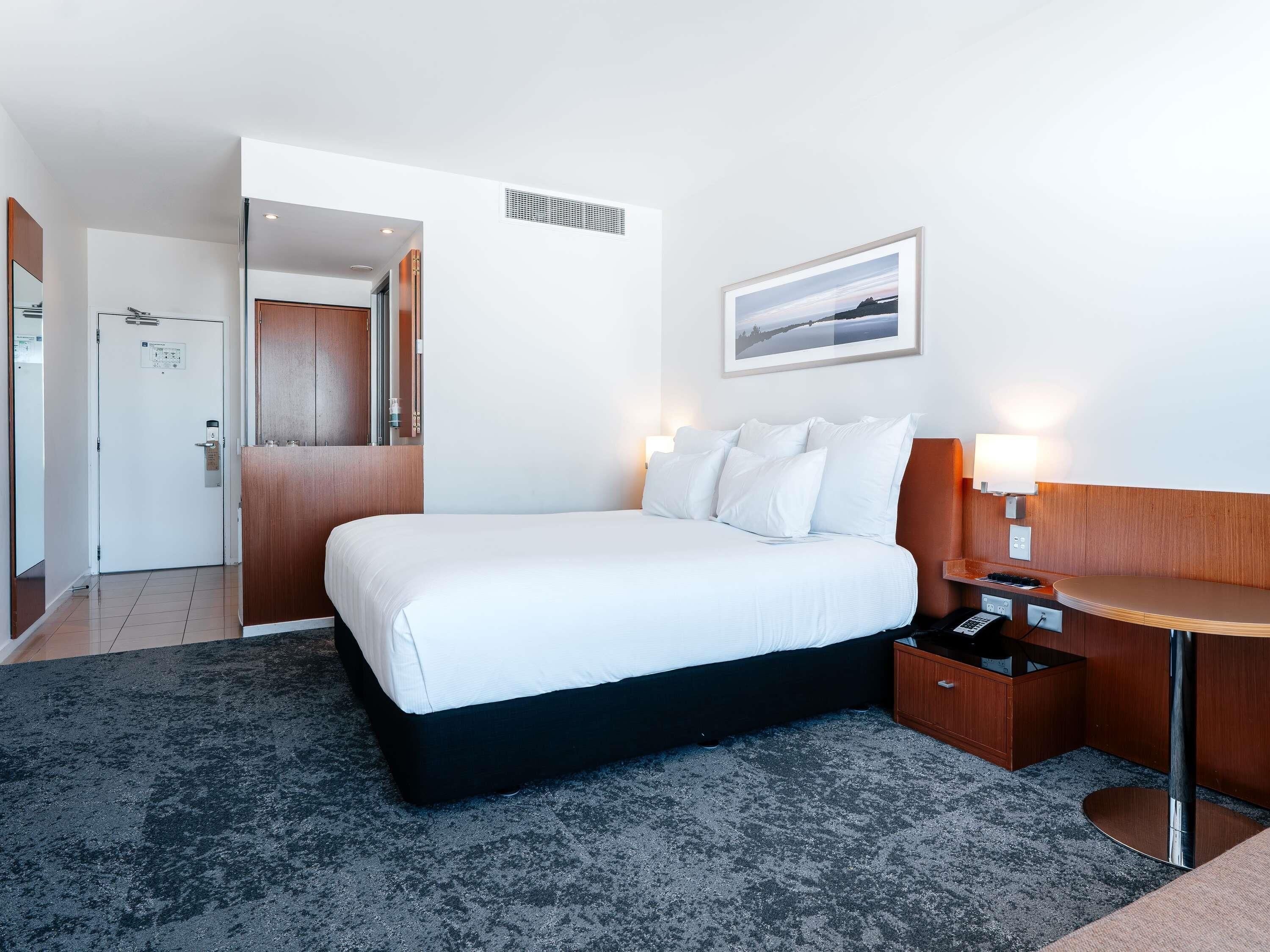 A hotel room with a bed, bedside table, lamp, and a picture on the wall.
