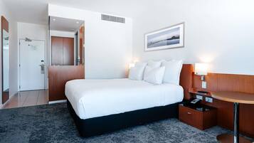 A hotel room with a bed, bedside table, lamp, and a picture on the wall.