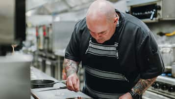 Un cocinero en una cocina con electrodomésticos de acero inoxidable y una tabla de cortar grande.