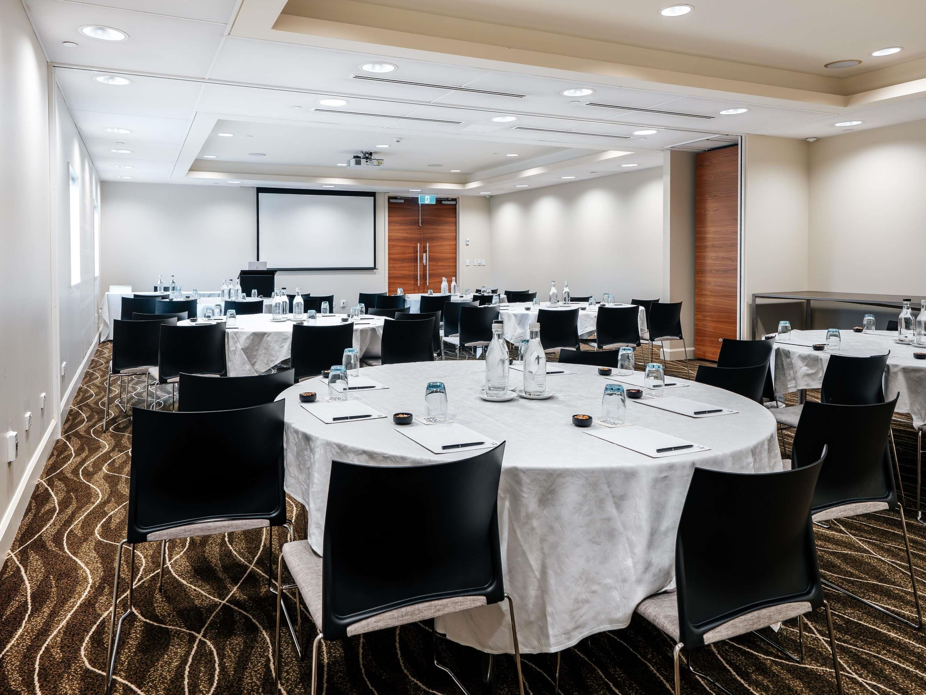 A conference room with multiple tables, chairs, and a projector screen.