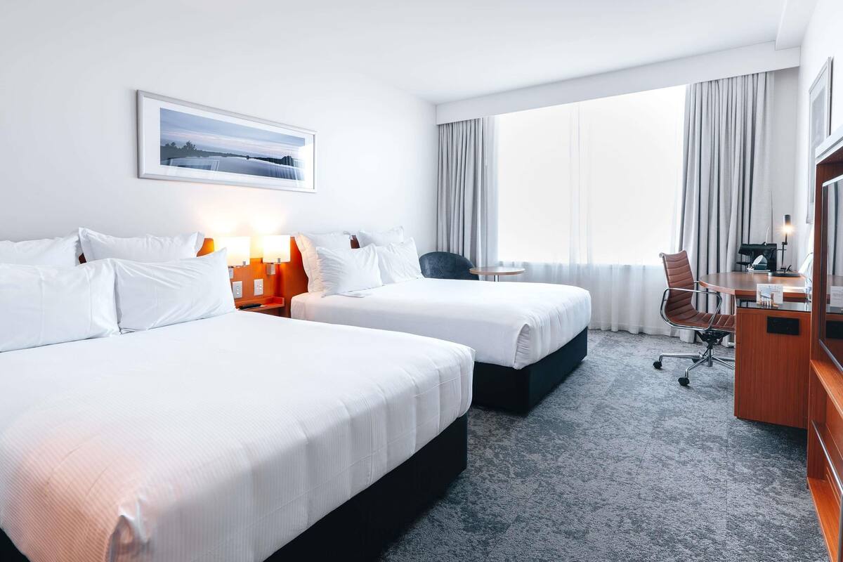 Ein Hotelzimmer mit zwei Betten, einem Schreibtisch, einem Stuhl und einem Fenster mit Vorhängen.