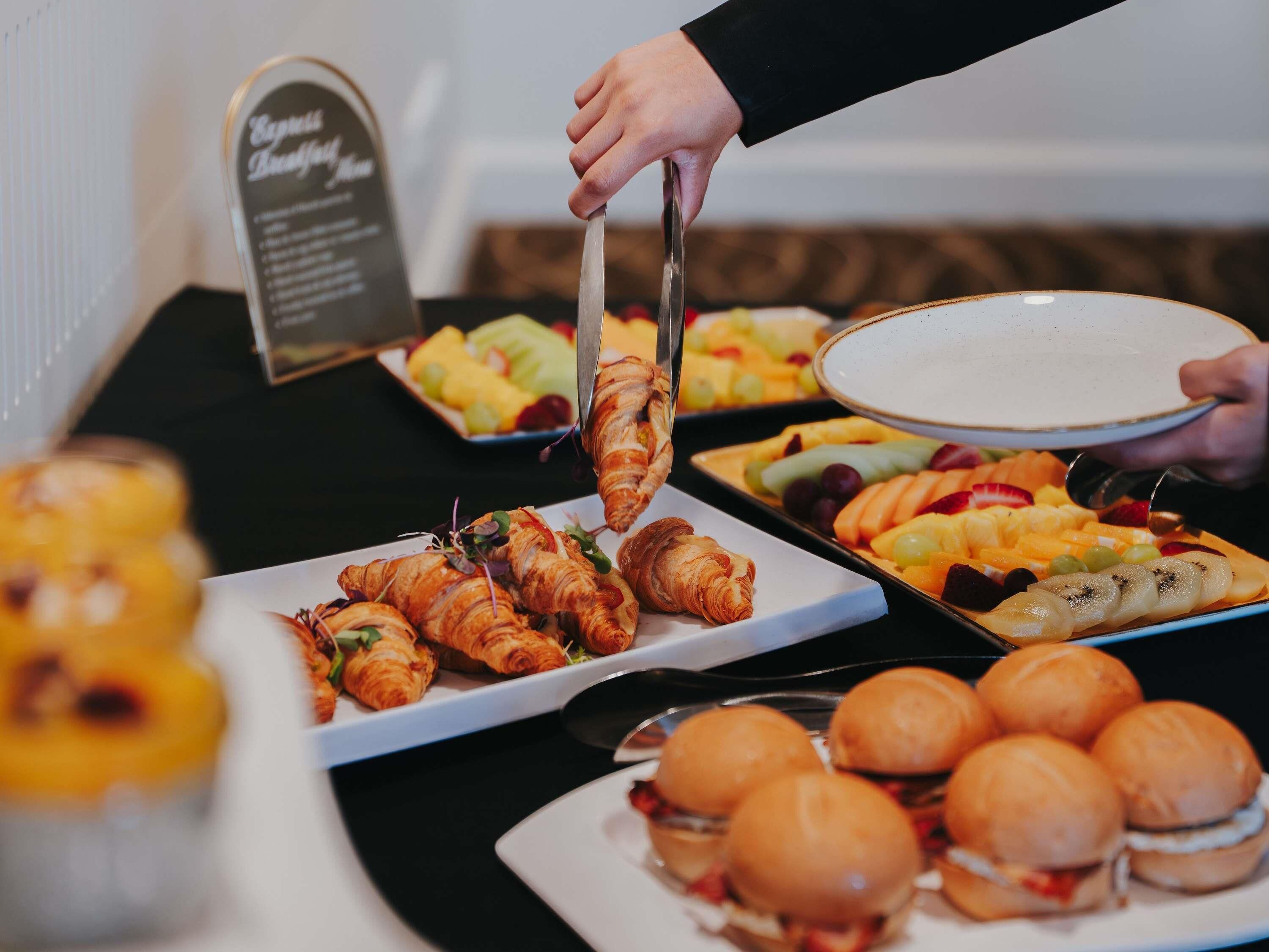 Een buffet met croissants, belegde broodjes en fruit.
